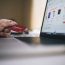 a hand holding a credit card in front of a laptop screen